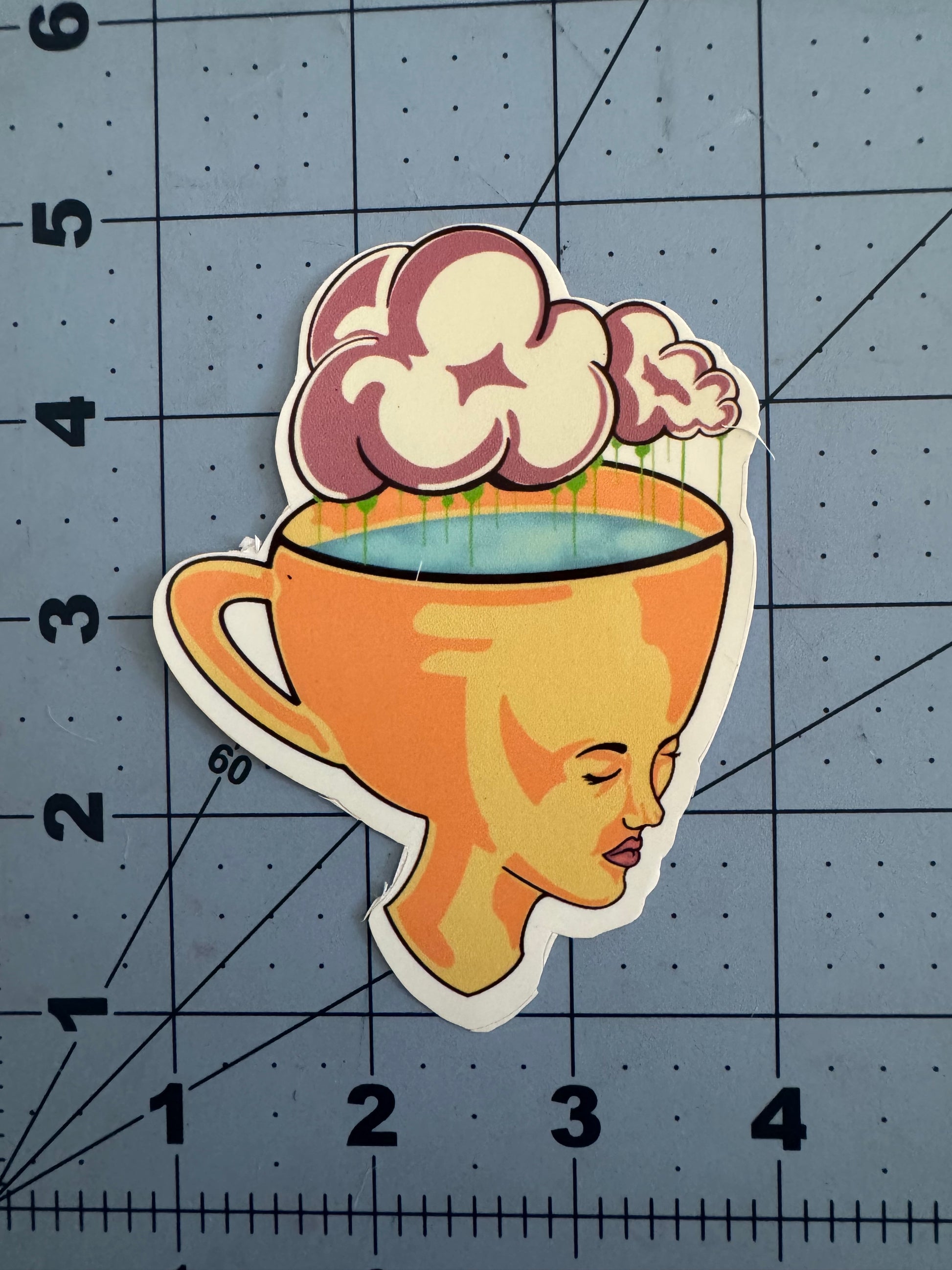 Sticker of a surreal illustration featuring an orange teacup with a human face on its side, eyes closed in peaceful contemplation. The cup is filled with a blue liquid and topped with fluffy pink clouds, with green rain dripping from the clouds into the liquid. The design blends dreamy and whimsical elements.